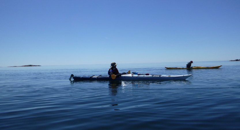 Two kayaks rest on the calm blue water of a vast lake with a clear blue sky above.